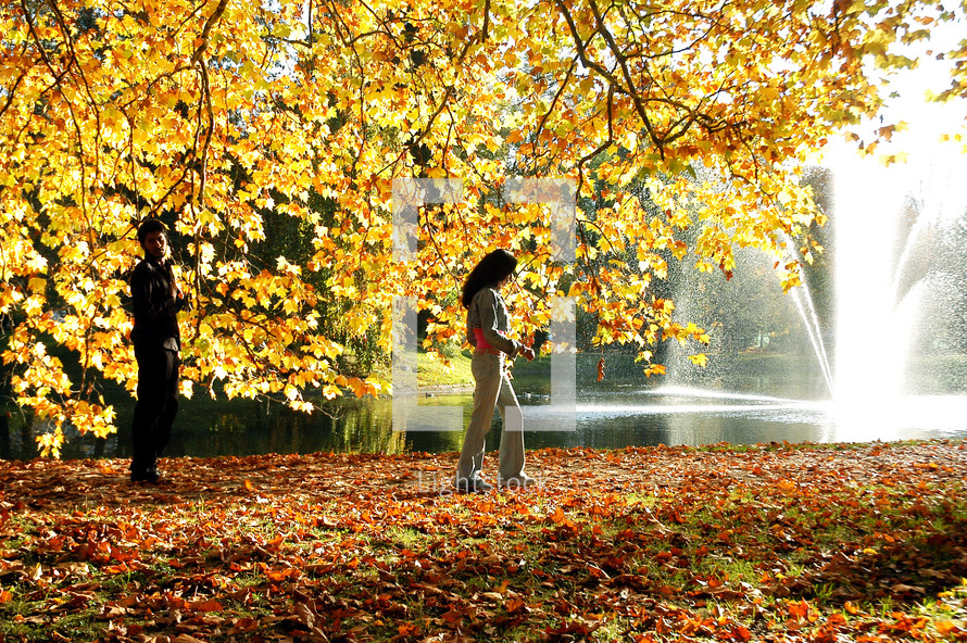woman walking under a fall tree and a fountain in a lake 