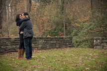 Man kissing woman on the cheek as they embrace in the park.