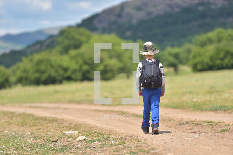 boy with backpack walking on a little path in mountains. Hiking kid