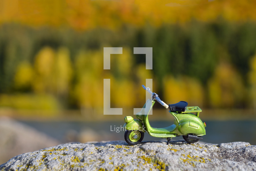 Small retro green scooter toy on a rock,