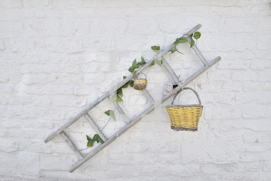 Wooden ladder with flowers and baskets against white painted brick wall in Alberobello, italy