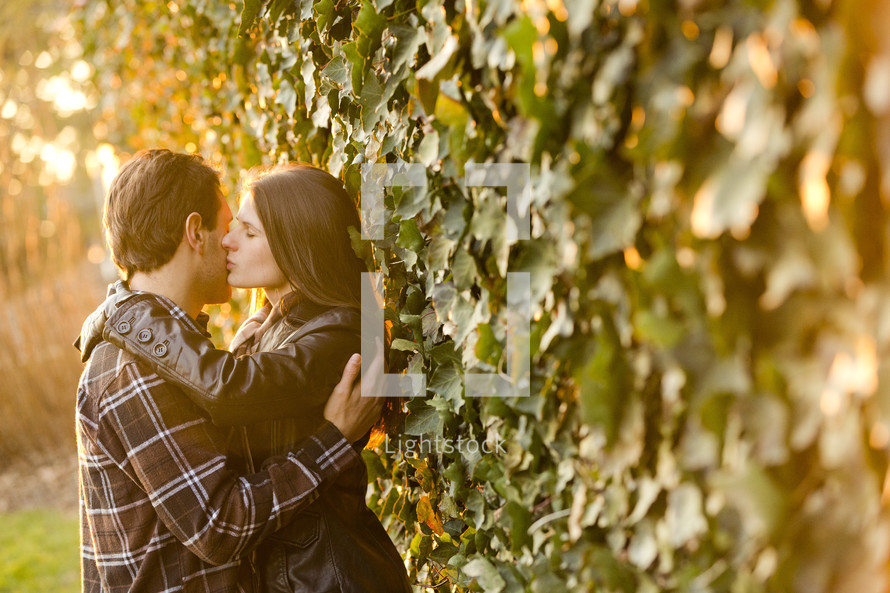 a couple kissing against an ivy covered wall