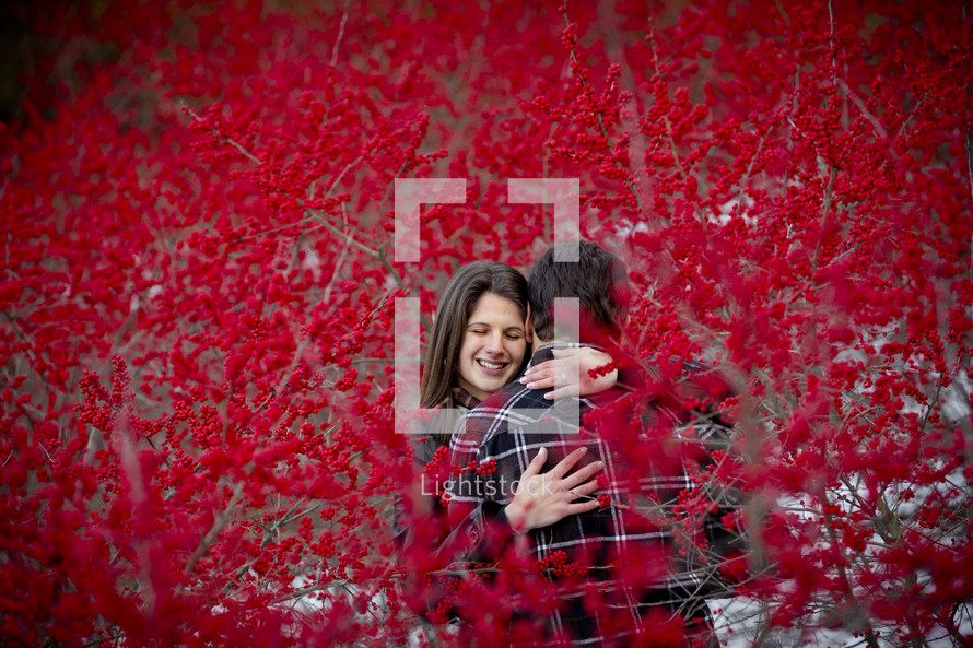 couple hugging between branches covered with red berries