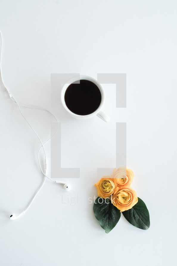 earbuds, coffee mug, and yellow flowers 