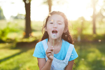 a girl blowing a dandelion 