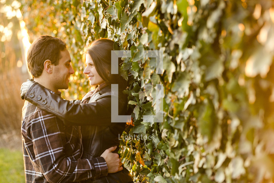 a couple looking into each others eyes standing against an ivy covered wall