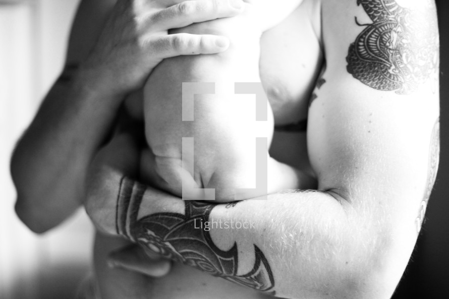 naked infant bottom resting on a father's tattooed arm