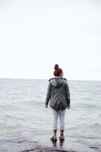 woman standing on rocks along a shore 