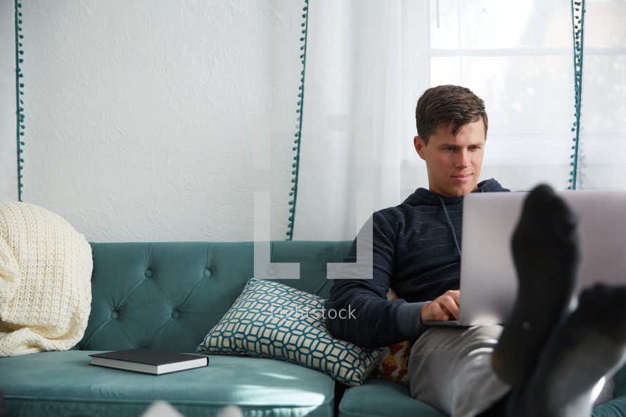 a man sitting on a couch working on a laptop 