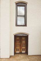 Wooden doors and a window in the front of a stucco building.