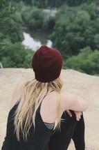 a woman in a wool cap sitting looking out at the river below 