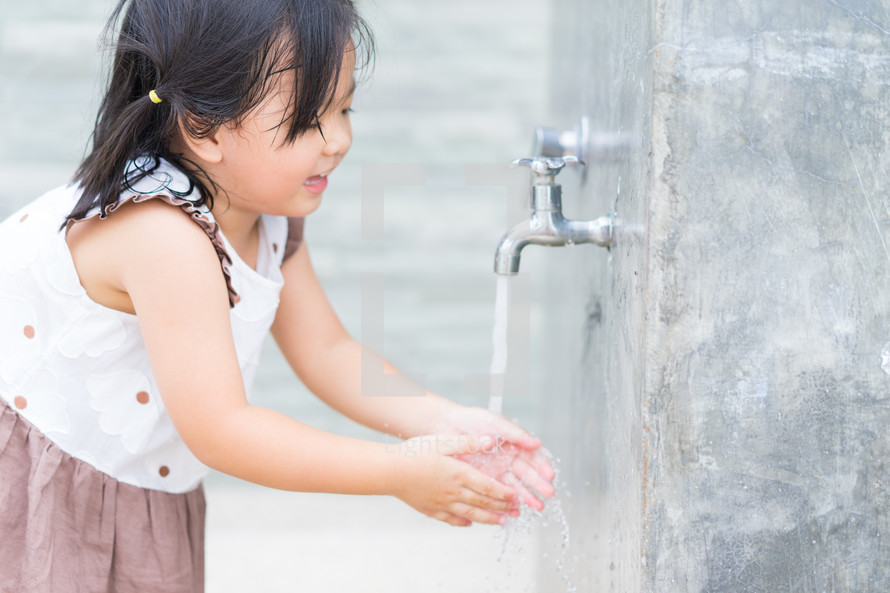 a child washing her hands under a spigot 