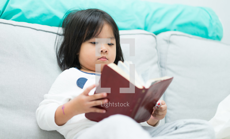 a child reading a book on a couch 