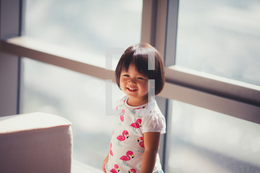 toddler girl standing in front of a window 