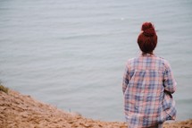 a woman sitting on a lake shore looking out a the water 