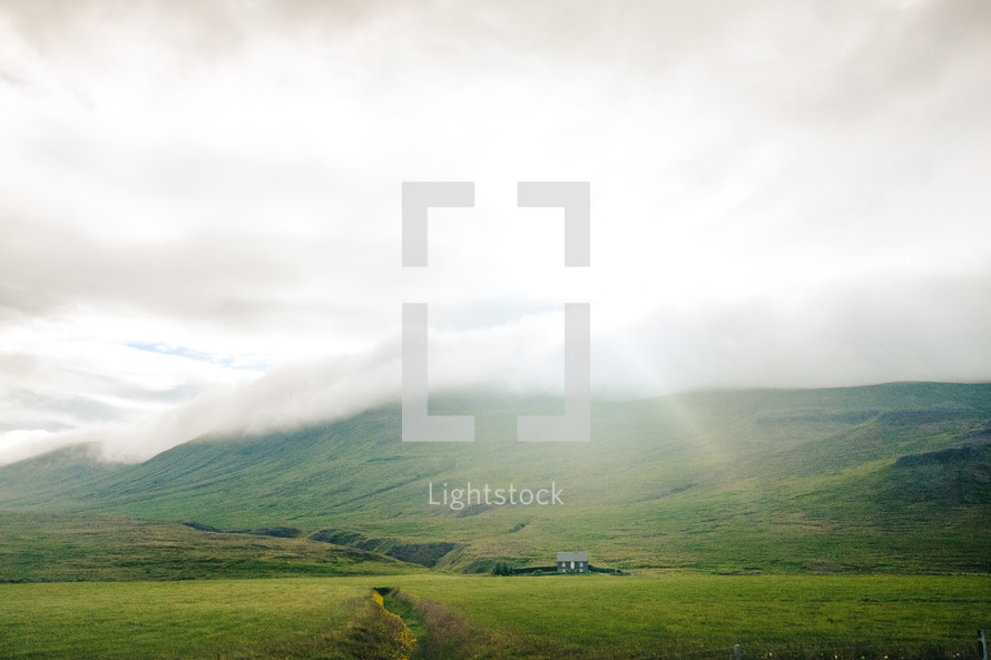 sunlight shining through clouds over a rural house in a valley 