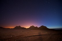 stars in the night sky over mountain peaks and desert landscape 