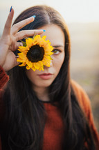 a woman holding up a yellow sunflower 
