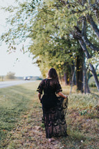 young woman in a black lace dress walking on the side of a road 
