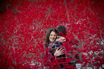 couple hugging between branches covered with red berries