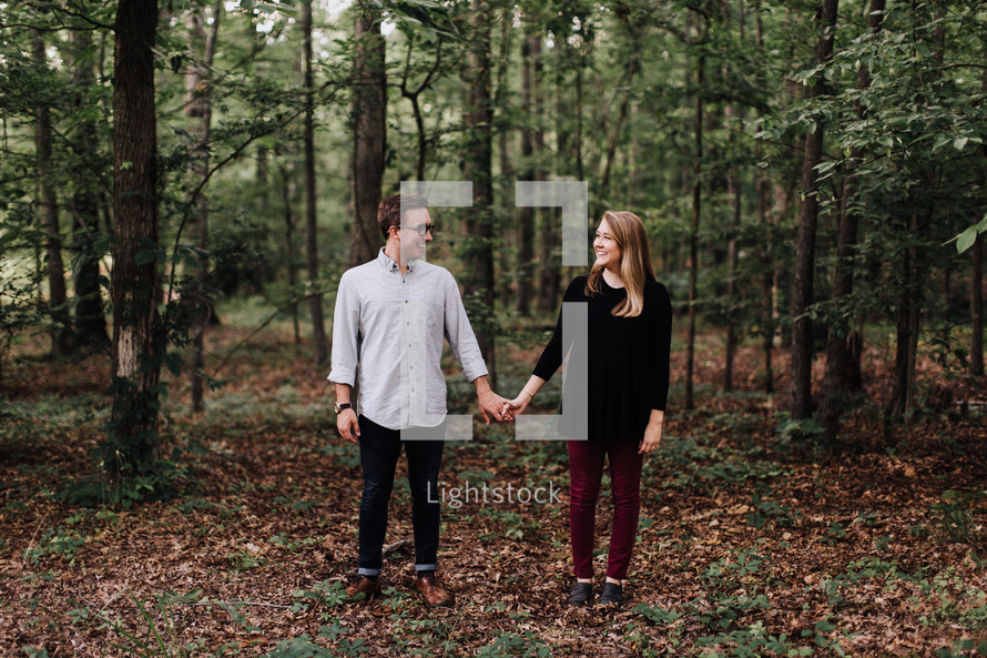 couple standing holding hands in the woods 