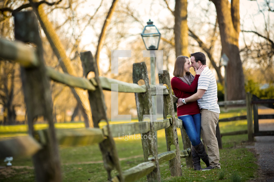 couple kissing outdoors leaning against a fence 