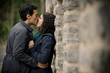 Woman leaning against stone wall kissing man facing her.