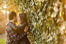a couple kissing against an ivy covered wall