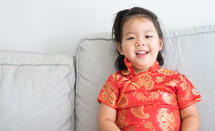 little girl in a traditional Chinese dress sitting on a couch 