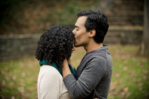 Man kissing woman on the head as they stand in a park.