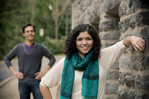 Smiling woman leaning on stone wall with smiling man standing with hands on his hips in the background.