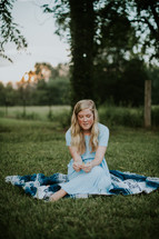 teen girl sitting on a blanket in the grass