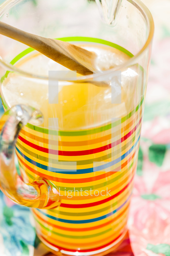 A striped pitcher full of lemonade wood spoon
