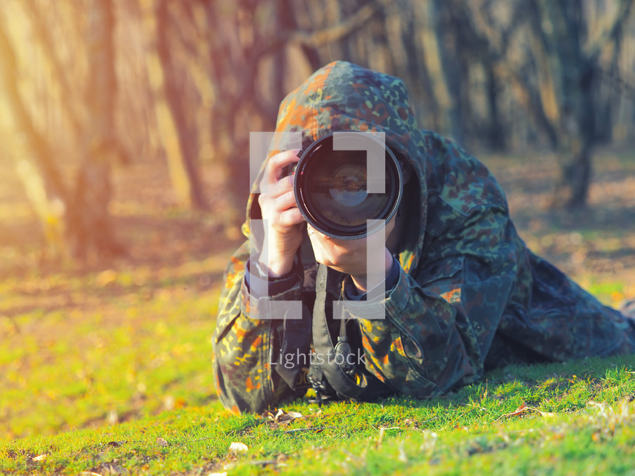 Wildlife photographer in camouflage outfit shooting, taking pictures