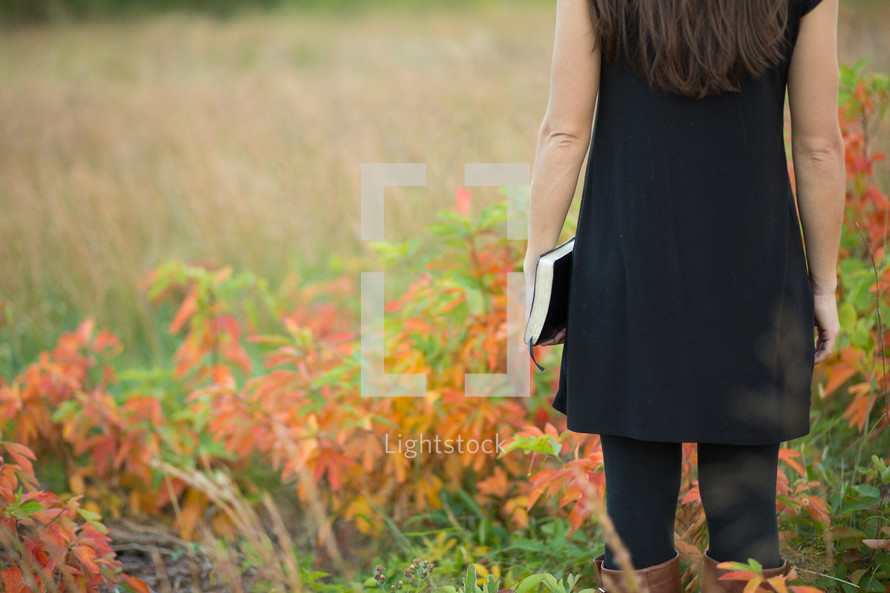 woman walking in a field holding a book