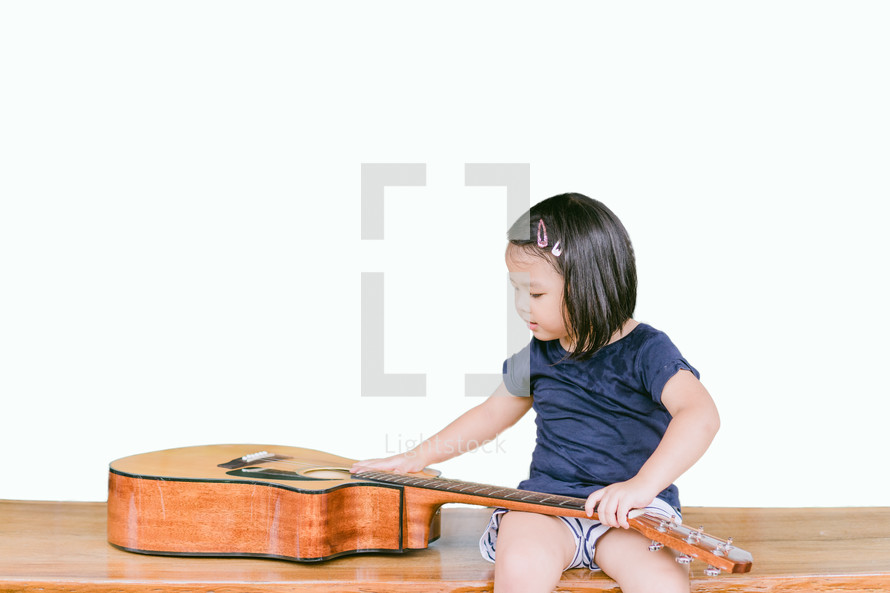 a toddler girl examining a guitar 