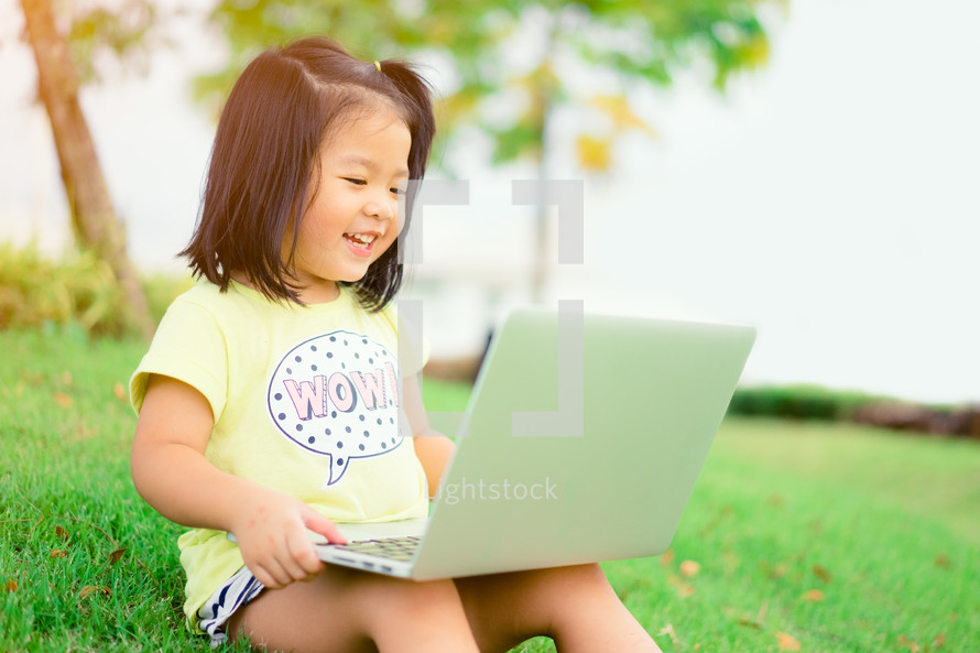 a toddler sitting in grass with a laptop on her lap 