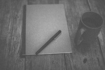 A pen and notebook next to a coffee mug