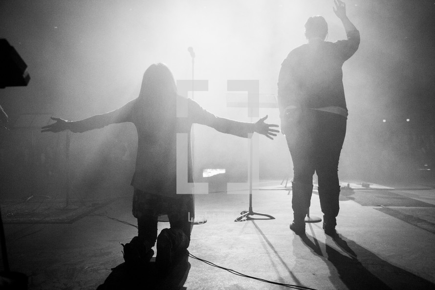 A woman on stage - arms wide open, on her knees, during a worship service
