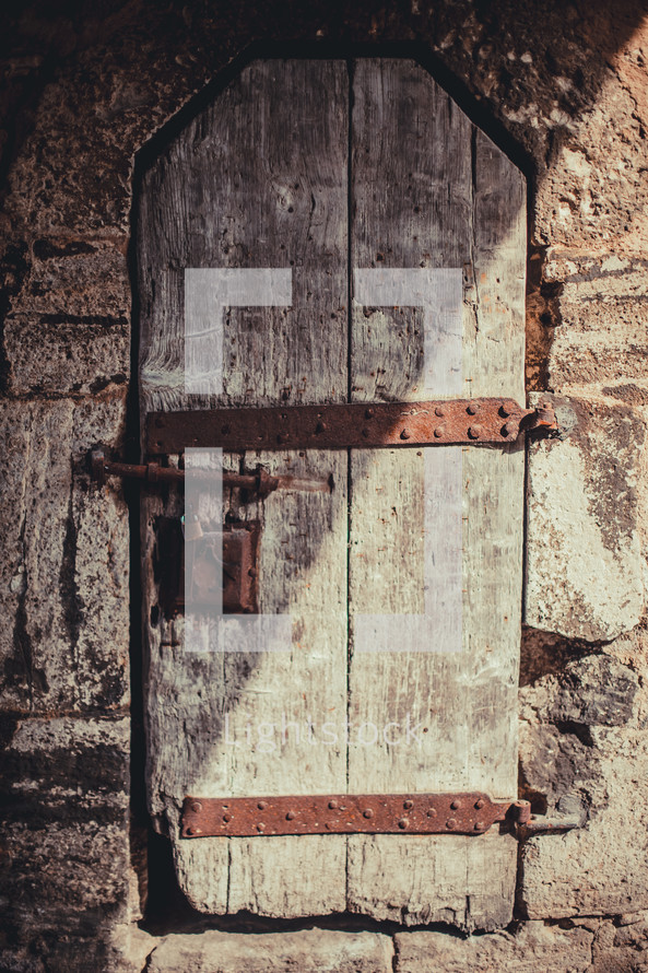 Old wooden door or window in a stone wall with rusted metal straps and lock, 