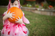 a little girl in a flamingo Halloween costume holding a pumpkin 