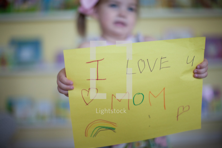a little girl holding a sign that reads I love mom 