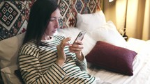 Young woman sitting on the bed scrolling on phone.