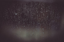 An abstract shot of rain droplets on a window with a dark moody background