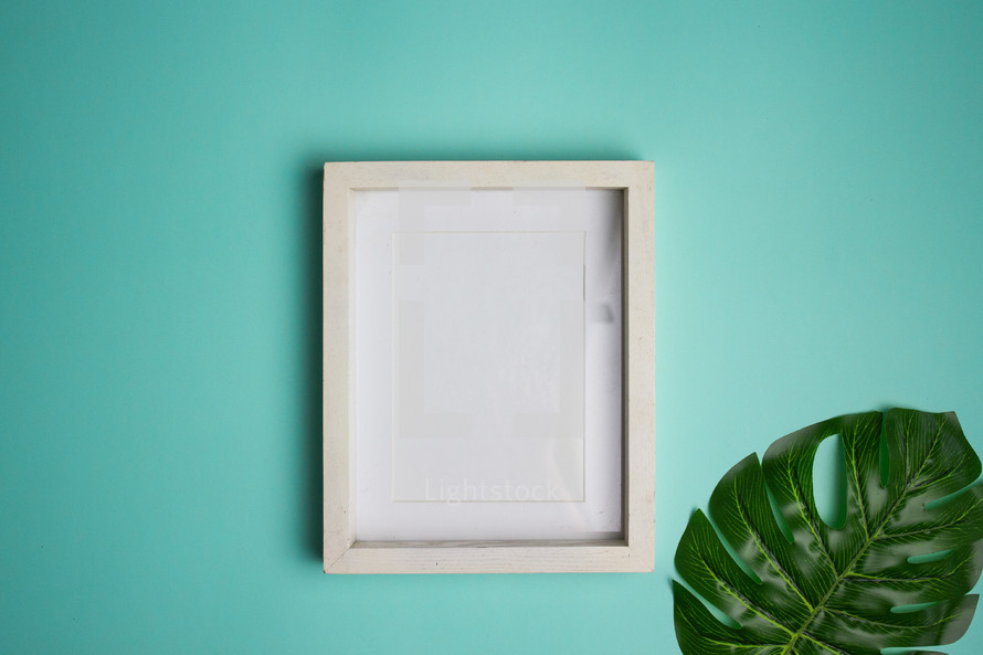 Blank white frame and leaf on turquoise background
