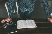 man resting his hands on a table reading a Bible