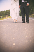 torso and legs of bride and groom standing on asphalt 