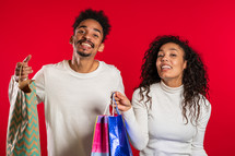 Happy young african couple with colorful paper bags after shopping isolated on red studio background. Seasonal sale, purchases, spending money on gifts concept.
