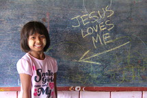 Jesus loves me on a chalkboard pointing to you a young girl in Myanmar