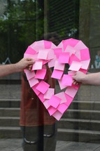 making a heart shape in sticky notes on a glass door 